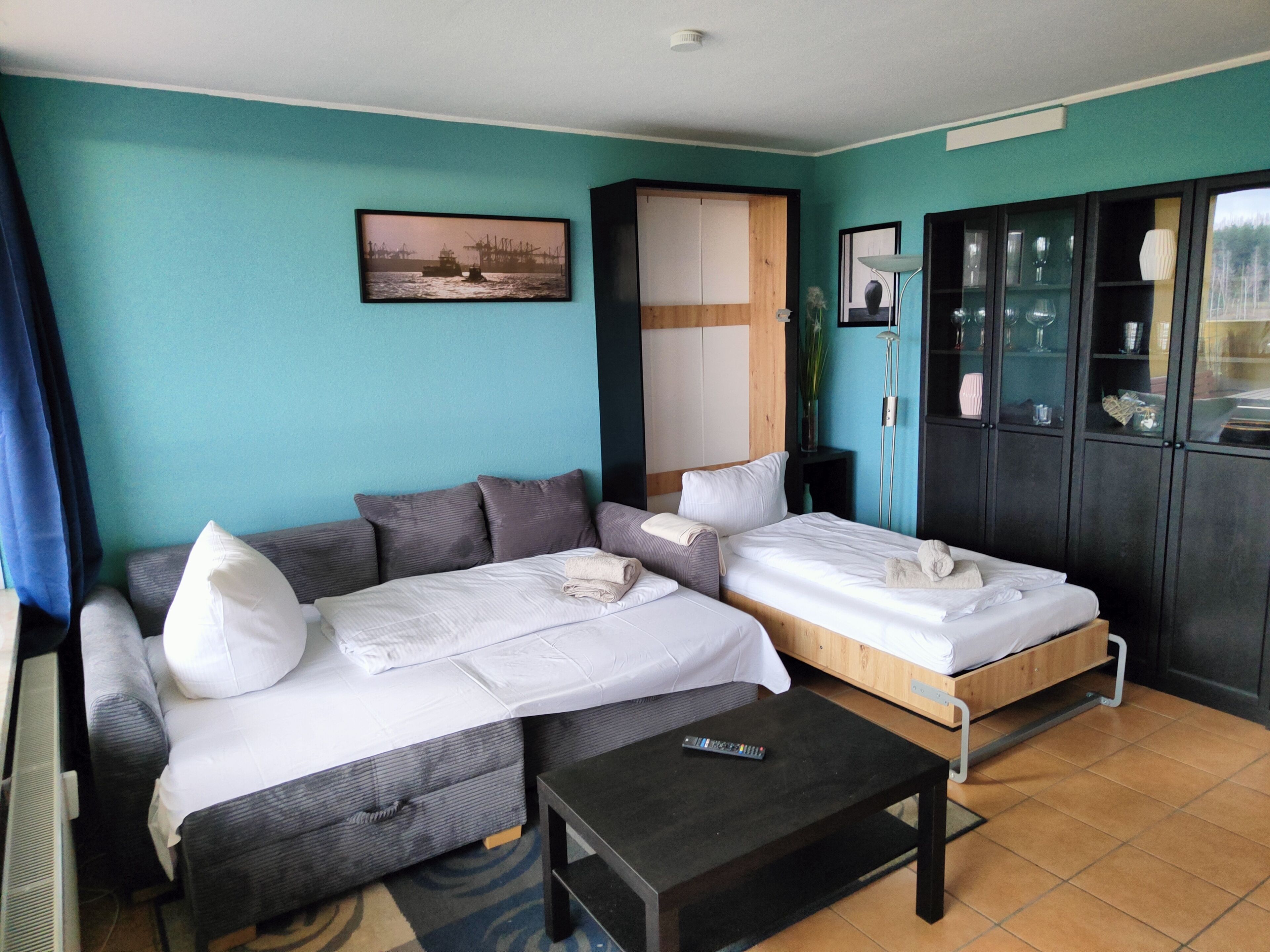 Une chambre d’hôtel avec deux lits, un canapé, une télévision et un meuble avec des portes en verre.