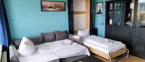A hotel room with two beds, a sofa, a TV, and a cabinet with glass doors.