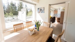 A dining area with a wooden table, chairs, a vase with flowers, and a basket of bread. - Apartments Harz Panorama (Braunlage)