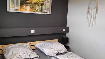 Ein Schlafzimmer mit einem Bett, das ein Baumast-Muster zeigt, einem Wand-Dreamcatcher und einem Gemälde mit Waldszene über dem Bett.