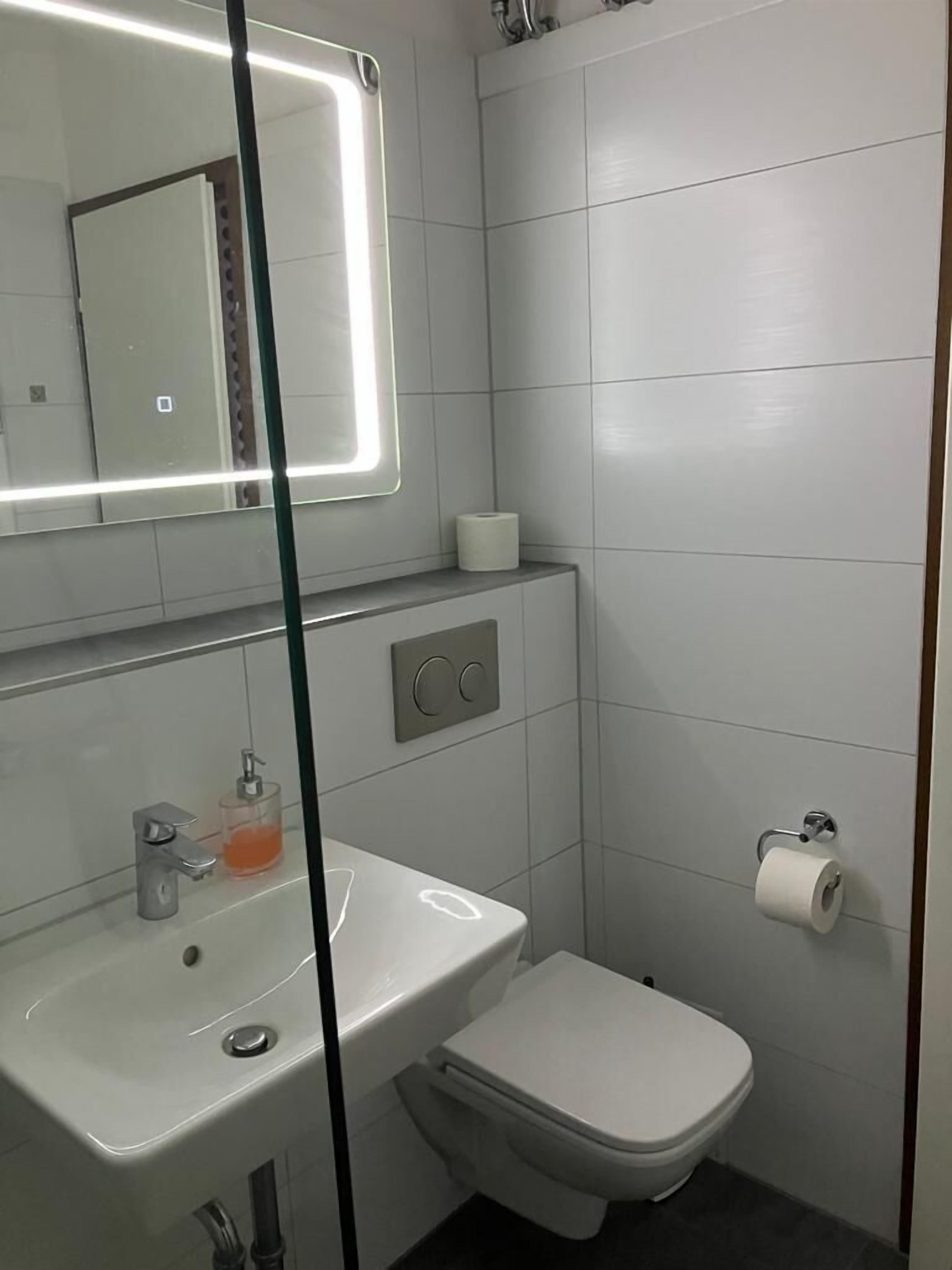 A bathroom with a white sink, a toilet, and a mirror with a light.