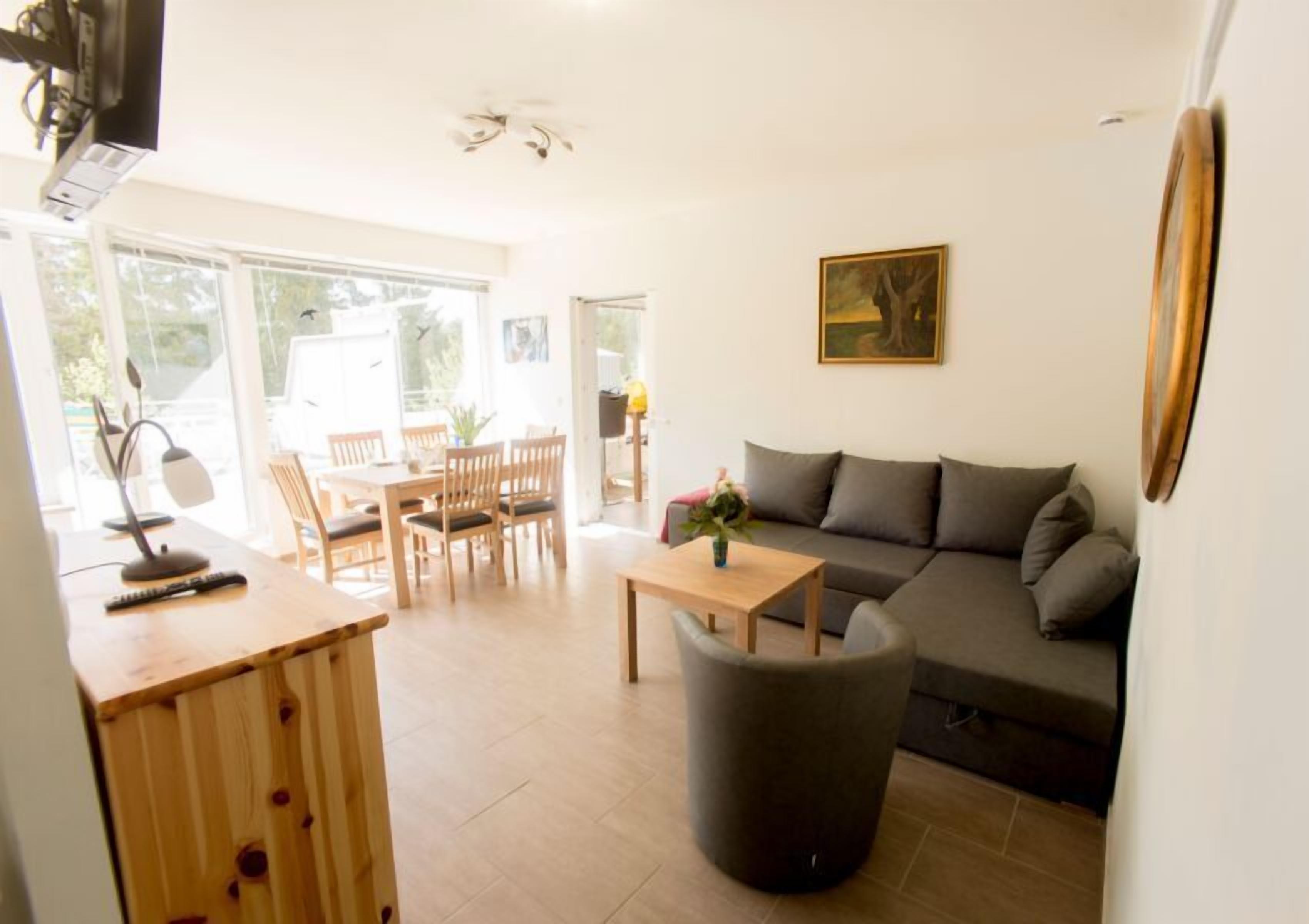 A modern living room with a sofa, a dining table with chairs, a small coffee table, and a large window providing natural light.