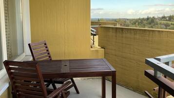 Un balcón con una mesa y sillas de madera, vista a un paisaje lejano y una pared amarilla.