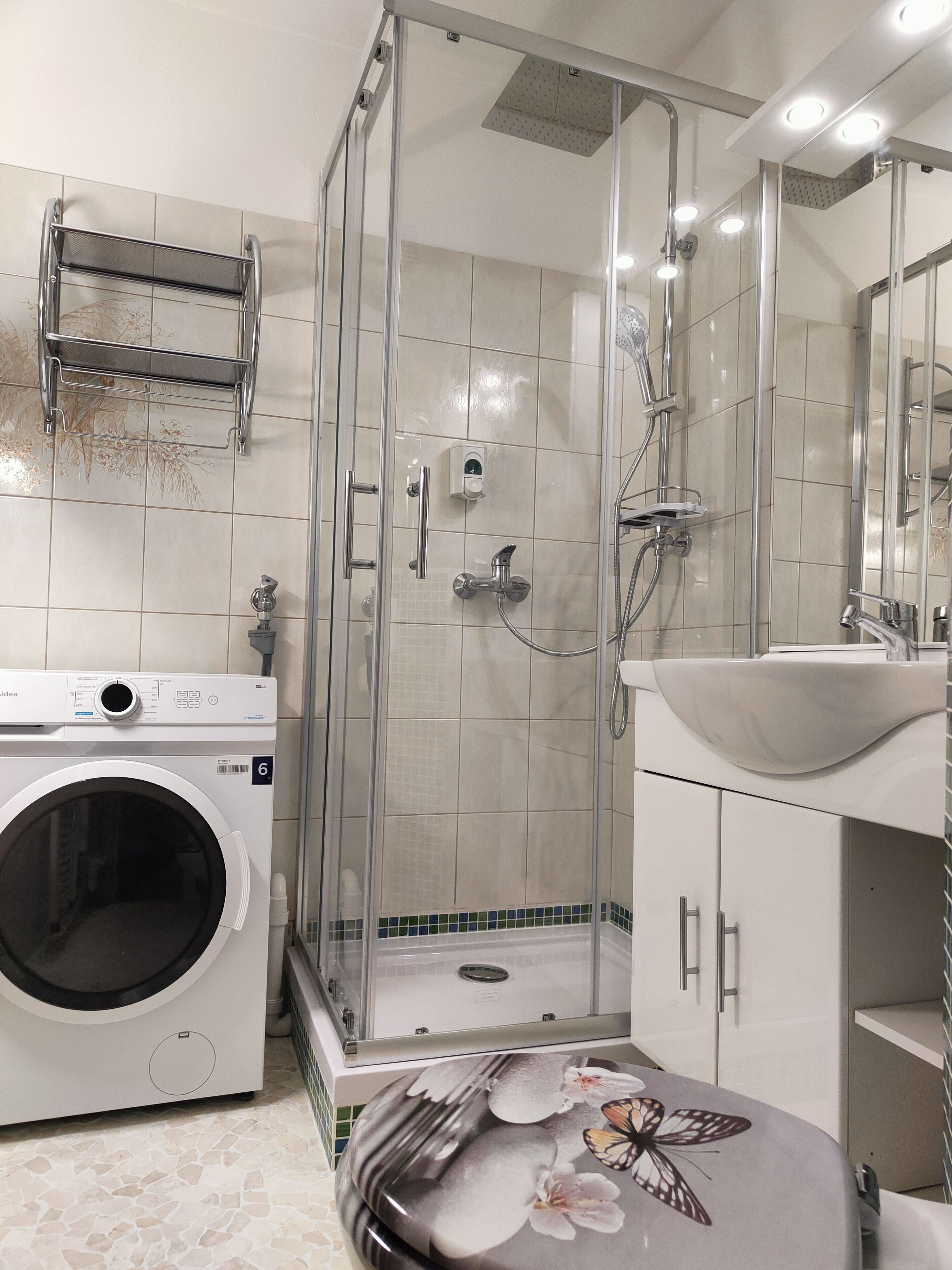 Une salle de bain moderne dotée d’une douche à parois de verre, d’un lave-linge encastré et d’un lavabo décoratif.