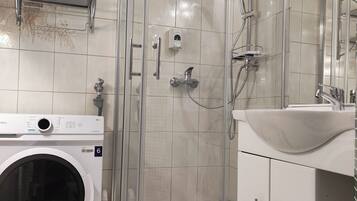 A modern bathroom with a glass-enclosed shower, a built-in washing machine, and a decorative sink.