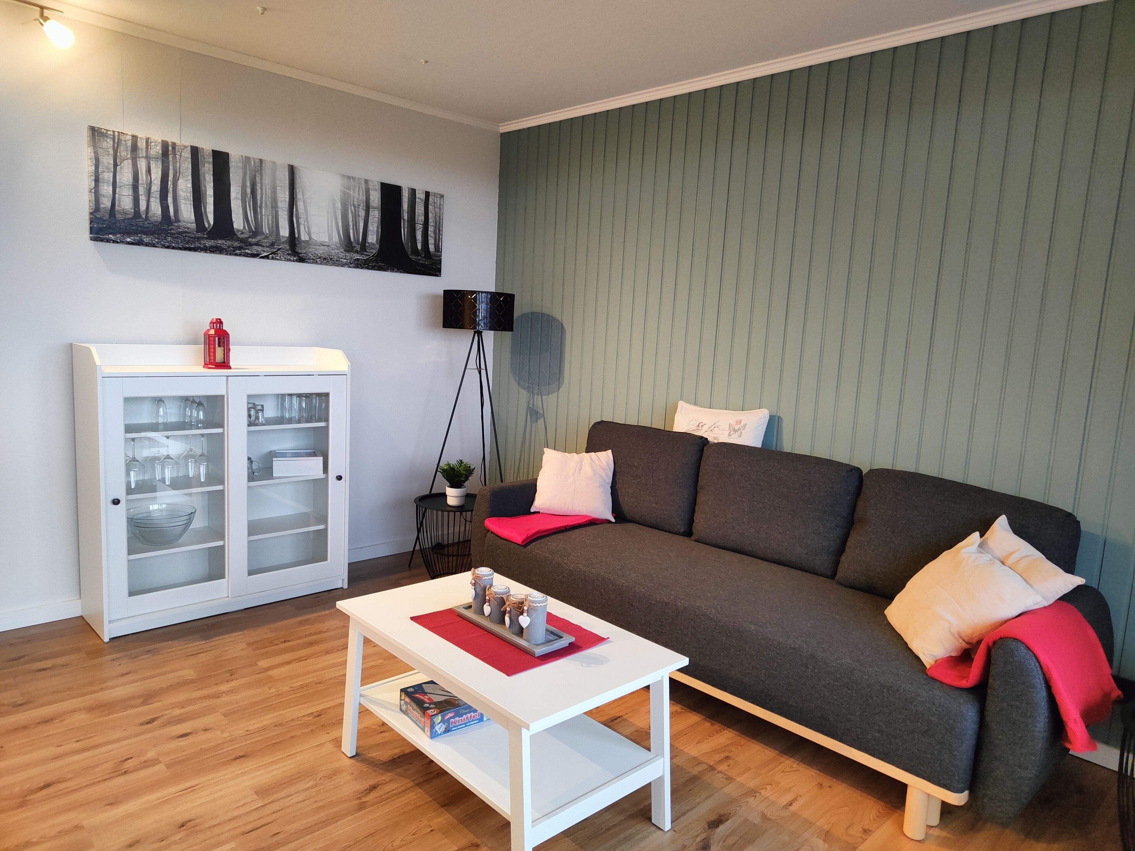 A living room with a dark grey sofa, white cushions, a red throw, a white coffee table, and a cabinet with glass doors.