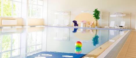 Una piscina con agua cristalina, un colchonete azul en la zona poco profunda y una pelota de colores.