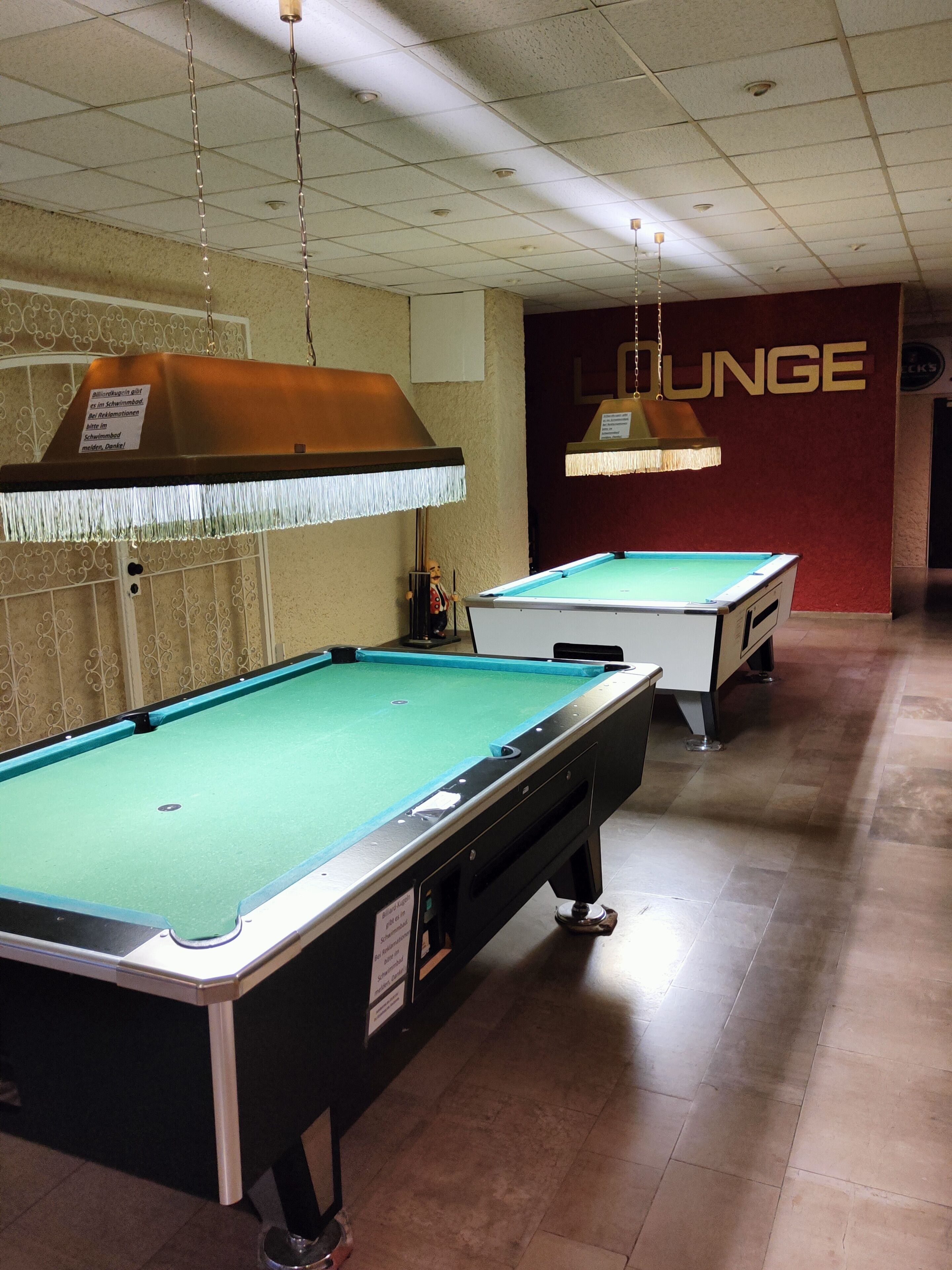 A pool table area with two pool tables, overhead lighting, and a wall with the word "LOUNGE".