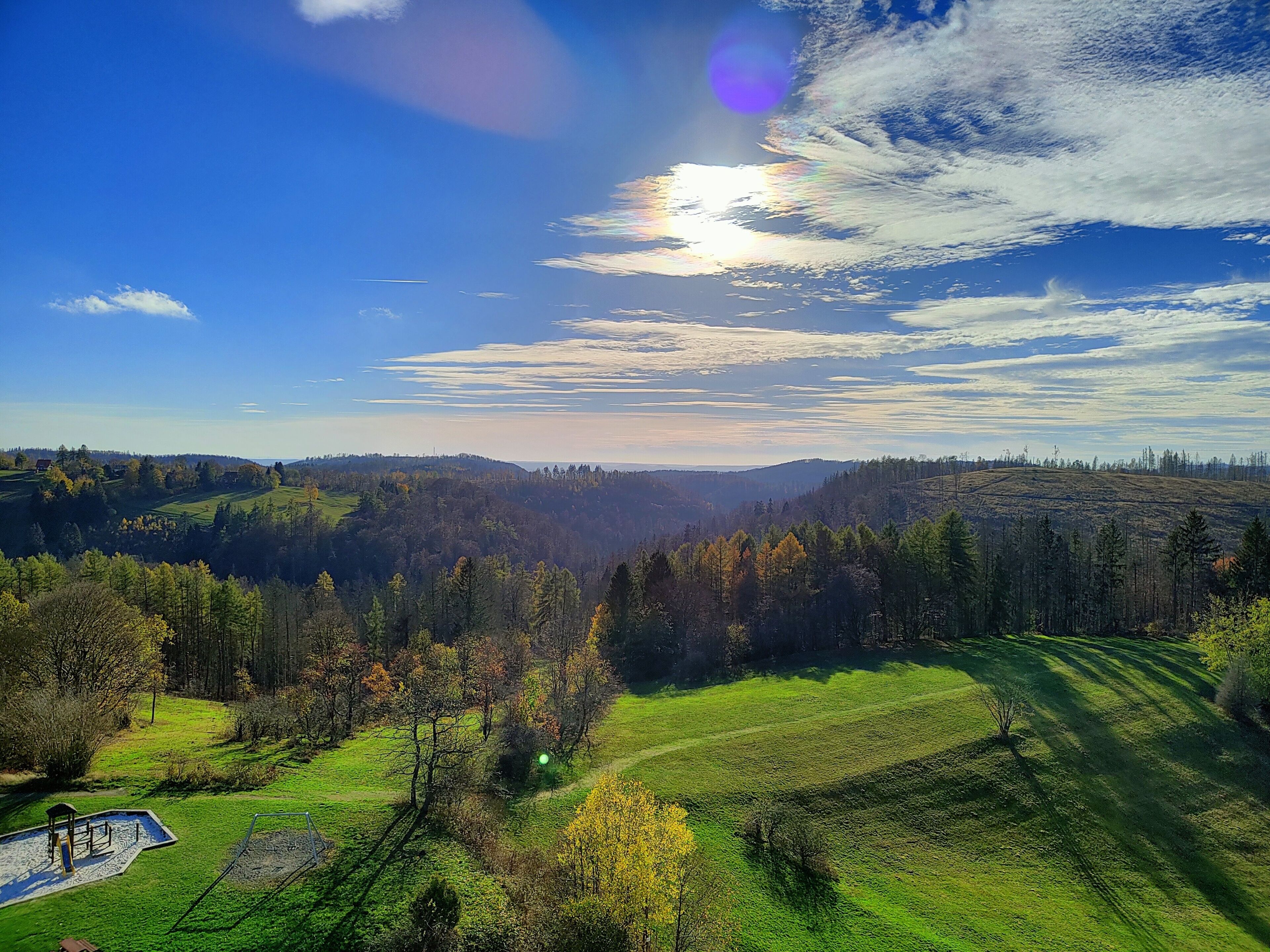 A panoramic view of a hilly landscape with a clear sky, a playground, and a small building.