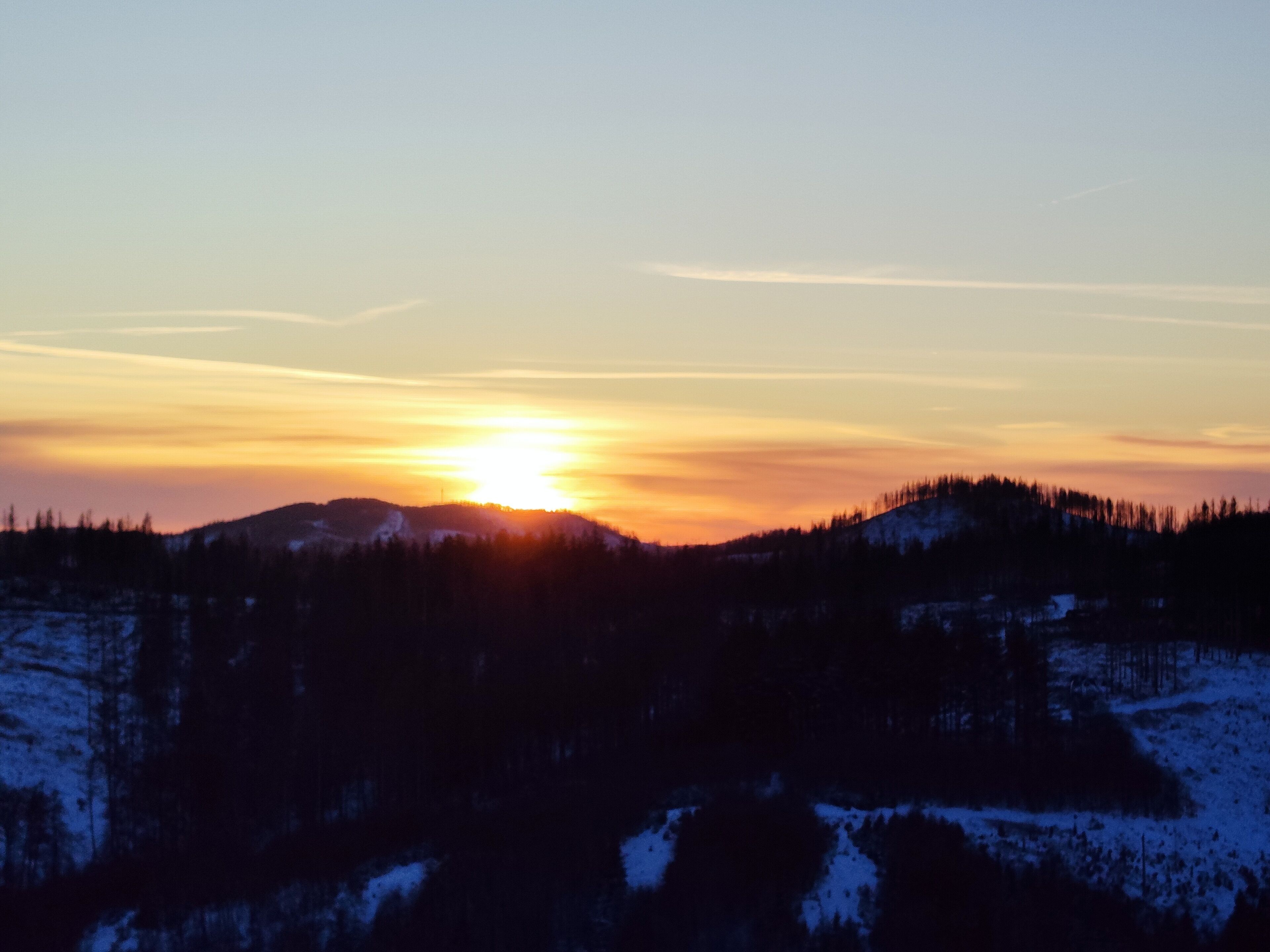A sunset over a snowy landscape with a forested hill.