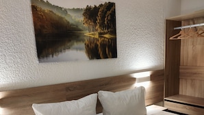 A bedroom with a wooden headboard, a bed with white bedding, and a painting of a lake scene on the wall. - Apartments Harz Panorama (Braunlage)
