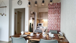 A dining area with a wooden table, four chairs, and a kitchen in the background. - Apartments Harz Panorama (Braunlage)