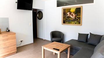 A modern living room with a grey sofa, a wooden coffee table, a black armchair, a TV mounted on the wall, and a painting.