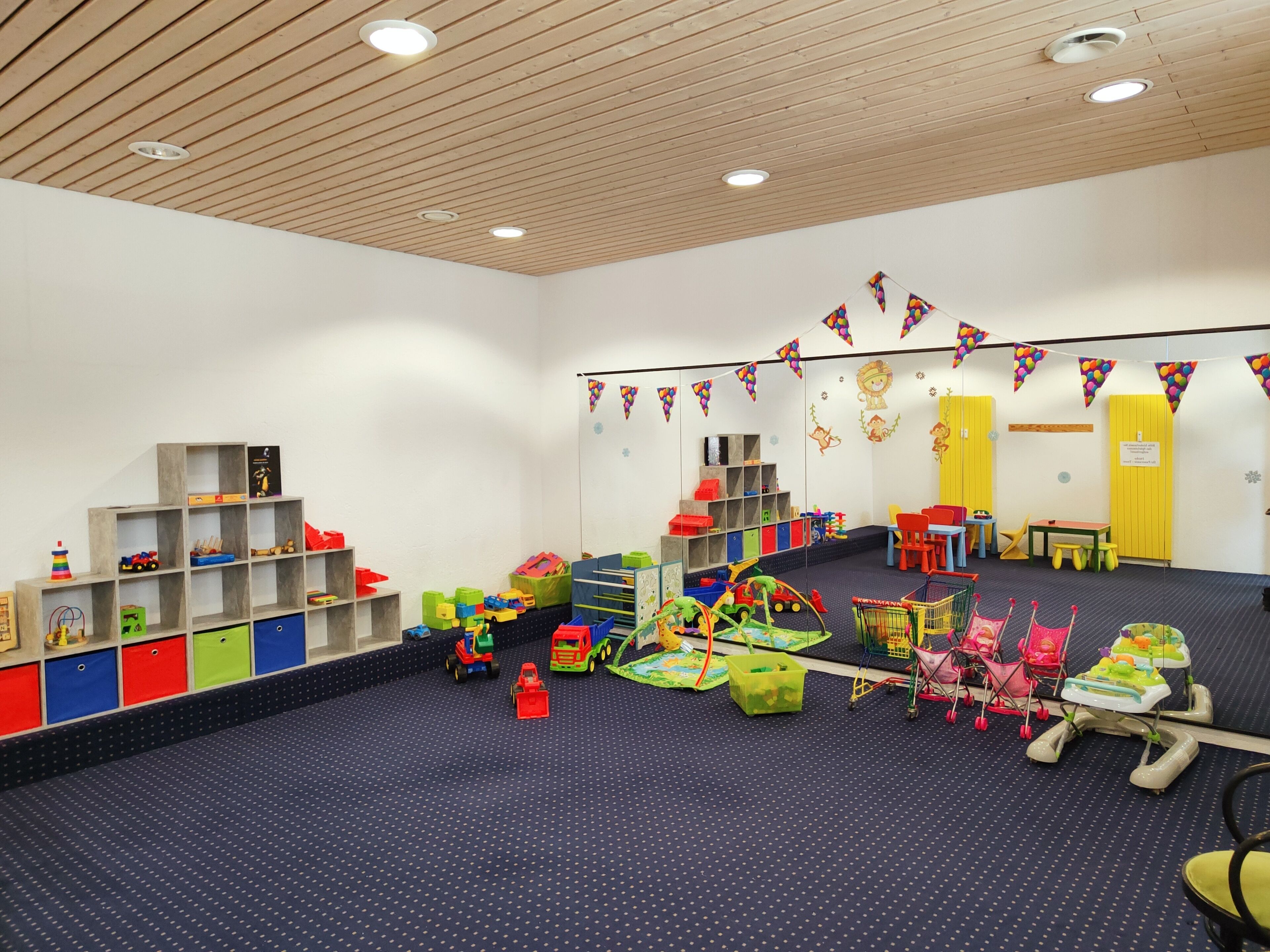 Una sala de juegos infantil con alfombra azul, estanterías de madera y juguetes de colores.