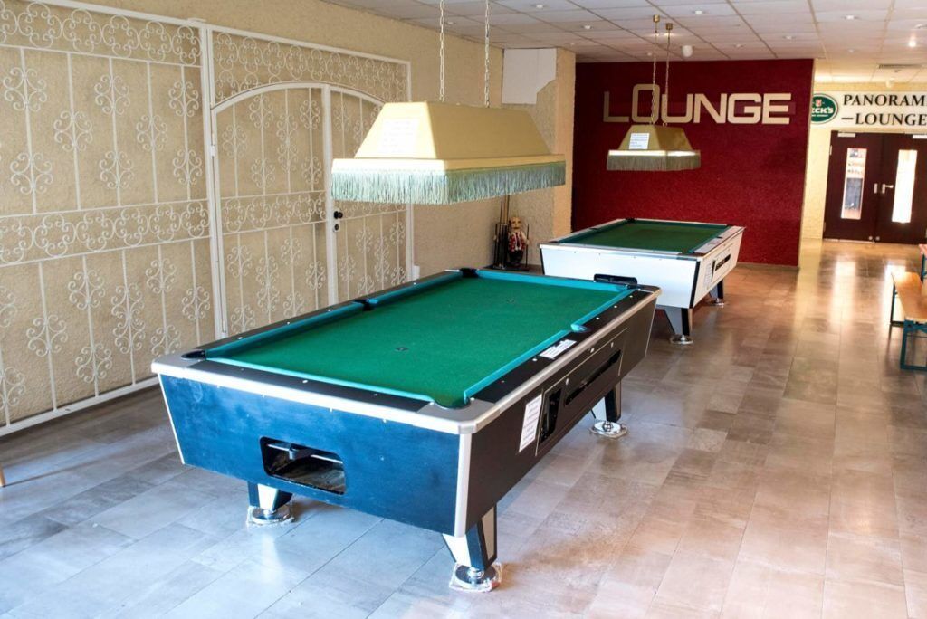 A pool table in a room with a patterned wall and a sign that reads "LOUNGE".