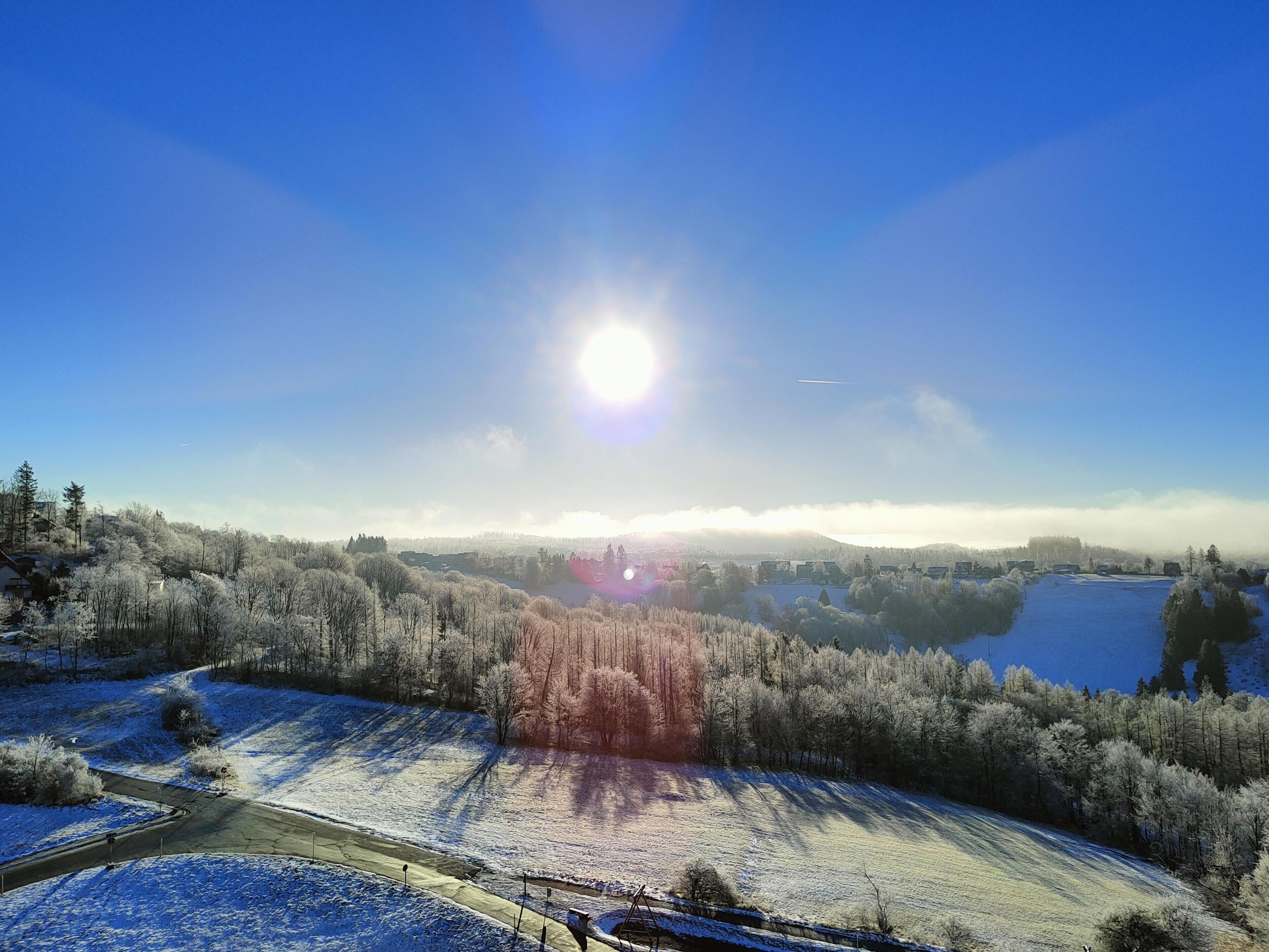 A panoramic view of a snow-covered landscape with a clear sky and a bright sun.