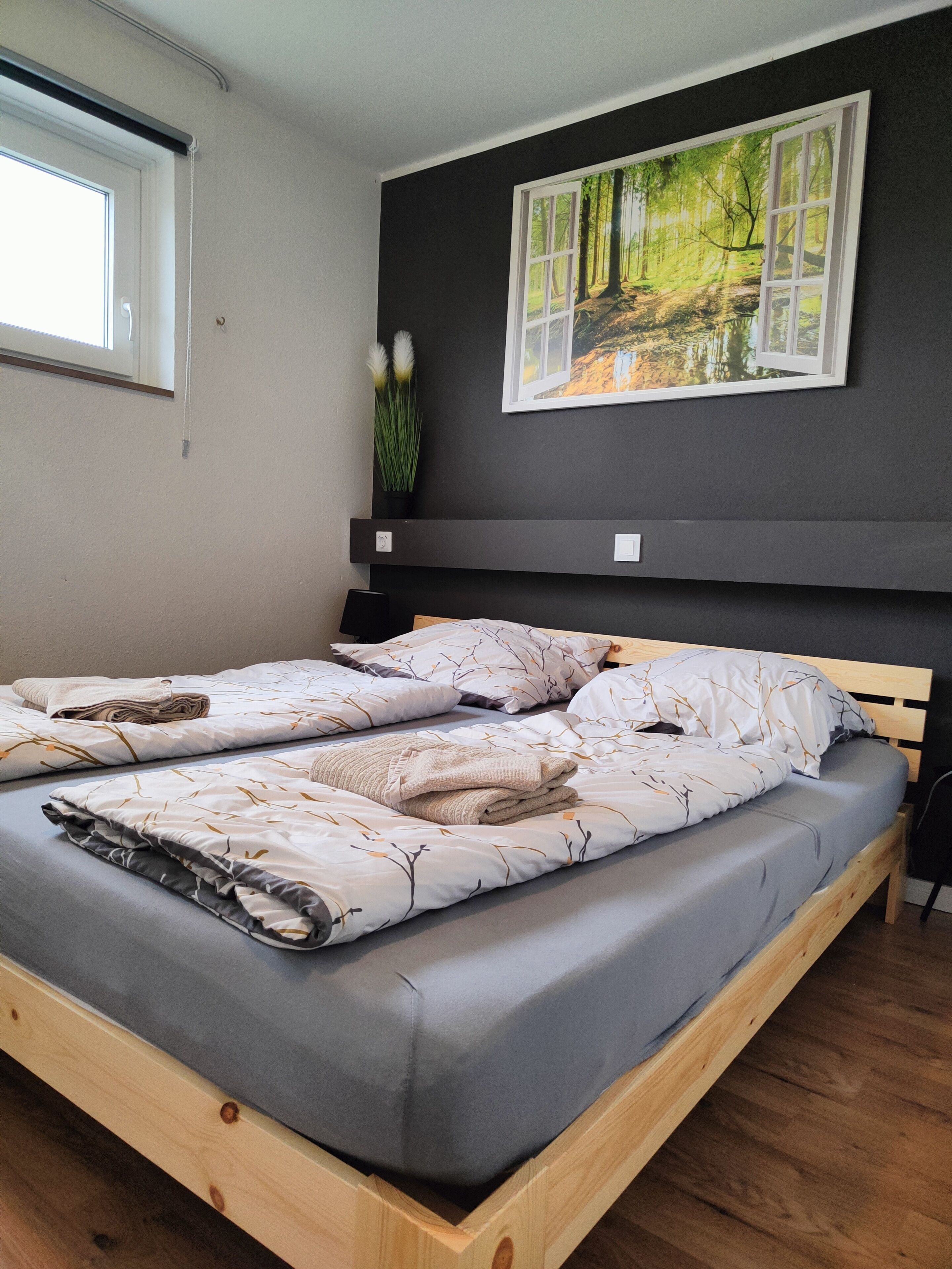 Une chambre avec un grand lit, une fenêtre, un tableau accroché au mur et une petite plante.