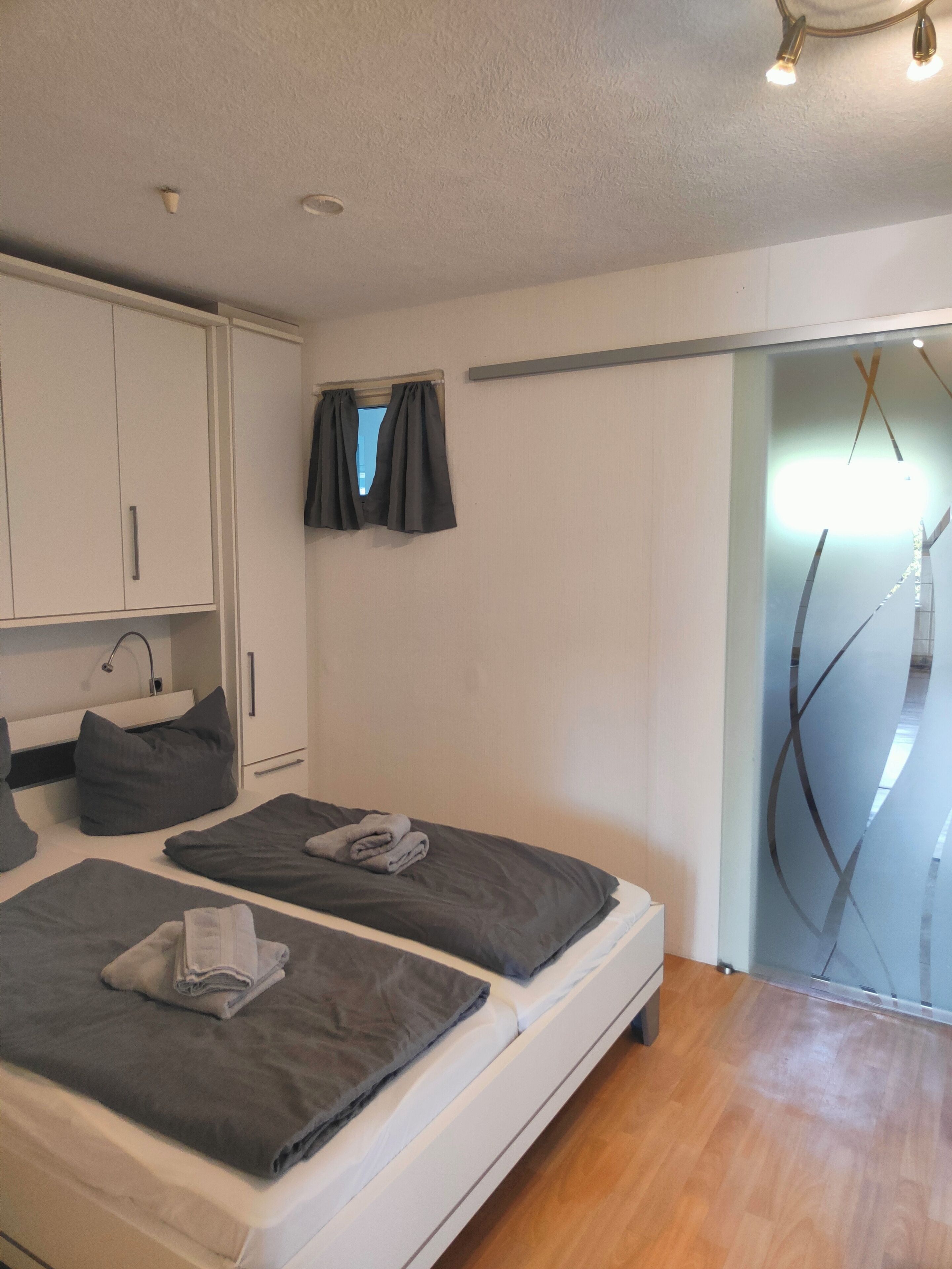 Camera da letto con due letti, un armadio, una finestra con tende e una porta che dà su un balcone.