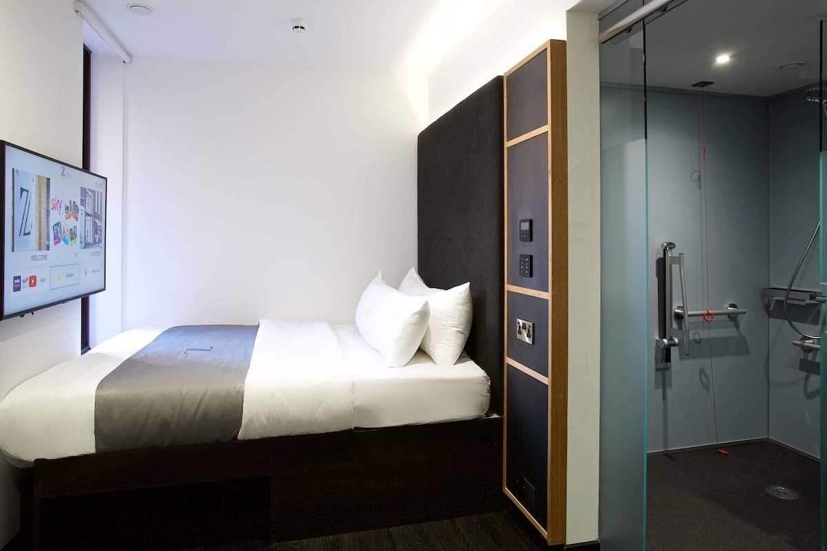 Une chambre d’hôtel moderne équipée d’un lit, d’un écran numérique affichant des informations sur la chambre et d’un espace douche.