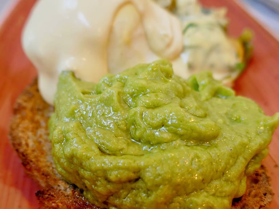 Un sándwich con guacamole y salsa cremosa sobre un plato rojo.