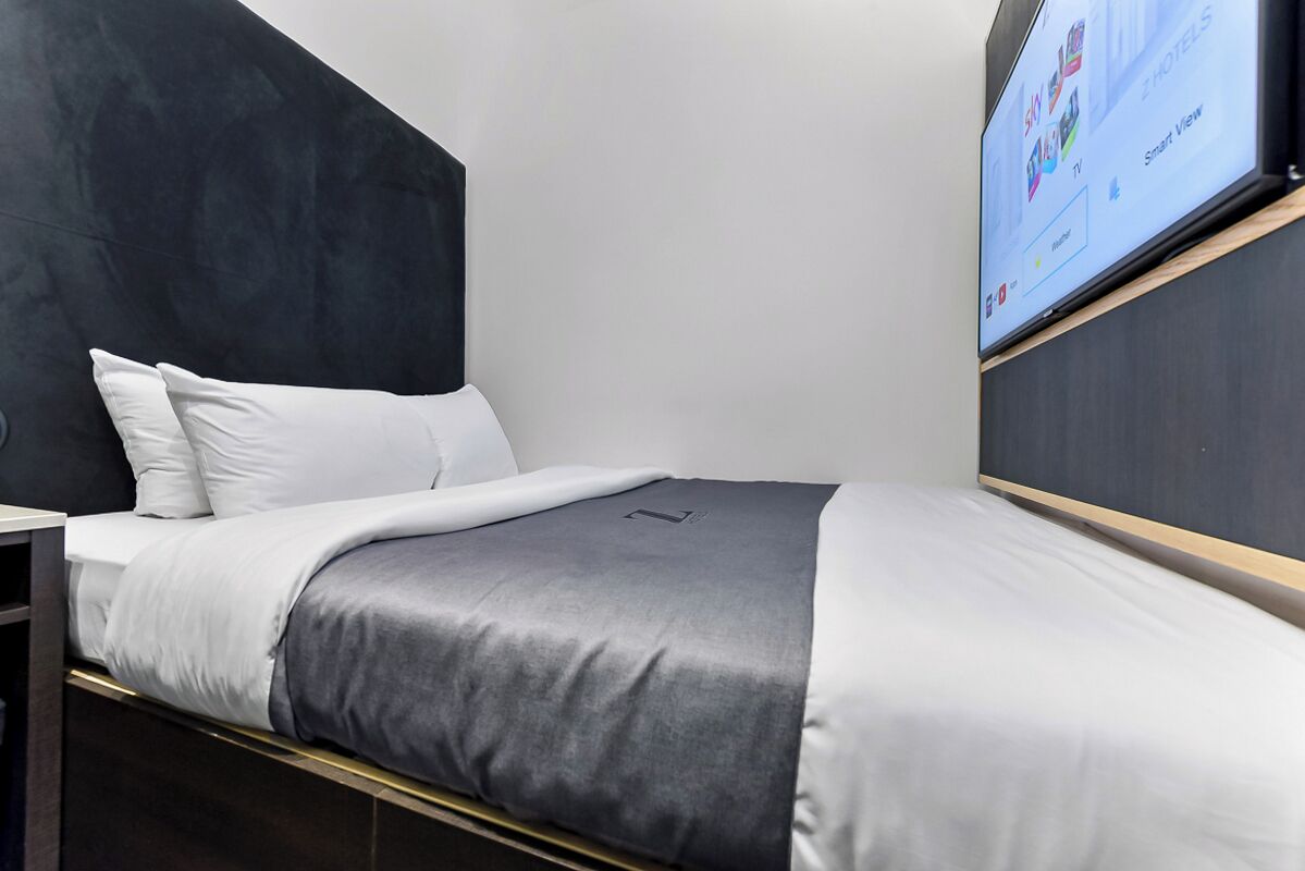 Een moderne hotelkamer met een bed, een aan de muur bevestigde televisie en uitzicht op de lucht.