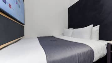 Ein modernes Hotelzimmer mit einem Bett, einem schwarzen Kopfteil, weißer Bettwäsche und einem an der Wand montierten Flachbildfernseher.