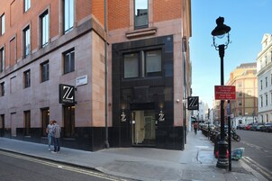 A hotel with a prominent 'ZL HOTELS' sign, a clear entrance, and a street view with parked cars and a pedestrian walkway.