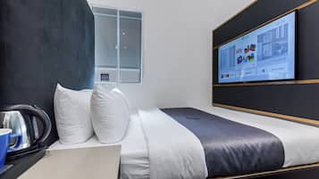 A modern hotel room with a bed, a flat-screen TV displaying the hotel's app, a window, and a kettle on the side table.