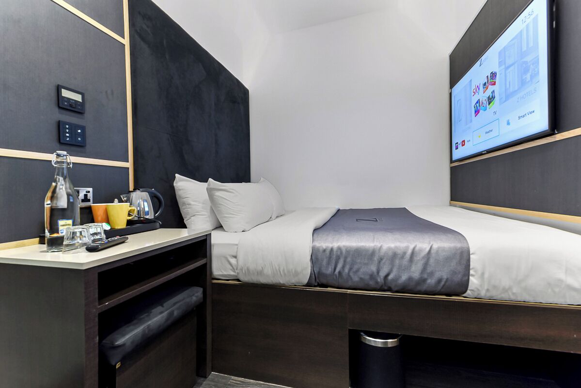 A modern hotel room with a bed, bedside table, and a TV mounted on the wall.
