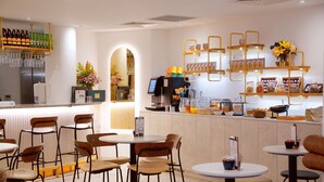 A cafe with multiple tables and chairs, a bar area with shelves of bottles and glasses, and a counter with a coffee machine and various food items. - The Z Hotel Trafalgar (London)