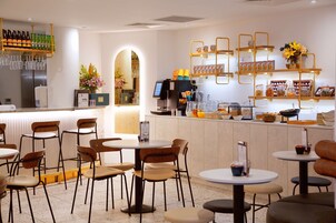 A cafe with multiple tables and chairs, a bar area with shelves of bottles and glasses, and a counter with a coffee machine and various food items.