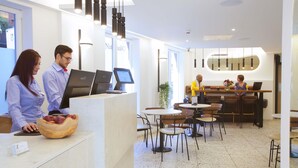 A modern hotel lobby with a reception desk, computers, and a seating area with tables and chairs. - The Z Hotel Trafalgar (London)