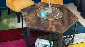 Ein Zimmer mit zwei gelben Stühlen, einem kleinen Holztisch, einer blauen Kerze und einem weißen Telefon an der Wand.