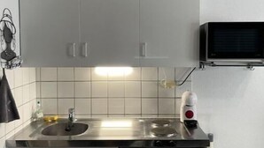 Eine kompakte Küche mit Edelstahlspüle, integriertem Mikrowellenherd und kleinem Kühlschrank.