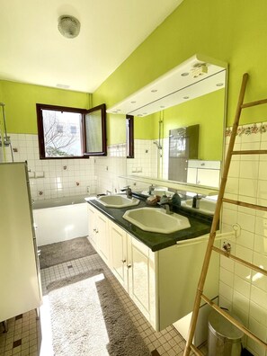 Une salle de bain avec deux lavabos, une baignoire, une fenêtre et un miroir.