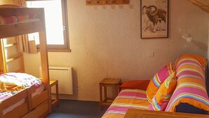 Ein gemütliches Dachzimmer mit Etagenbett, Holztisch und farbenfroher, gestreifter Bettdecke.
