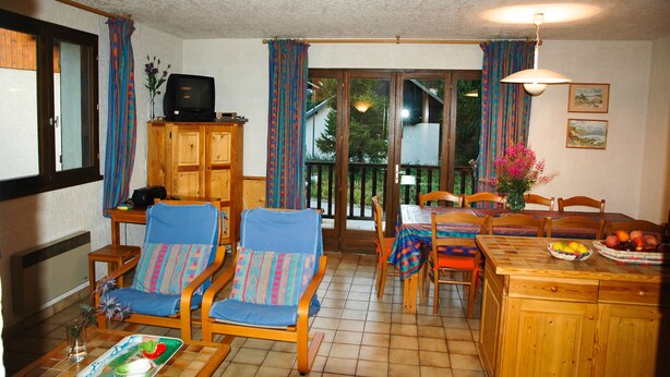 Ein gemütliches Wohnzimmer mit Fernseher, Holzmöbeln und einem Essbereich mit Tisch für zwei Personen.