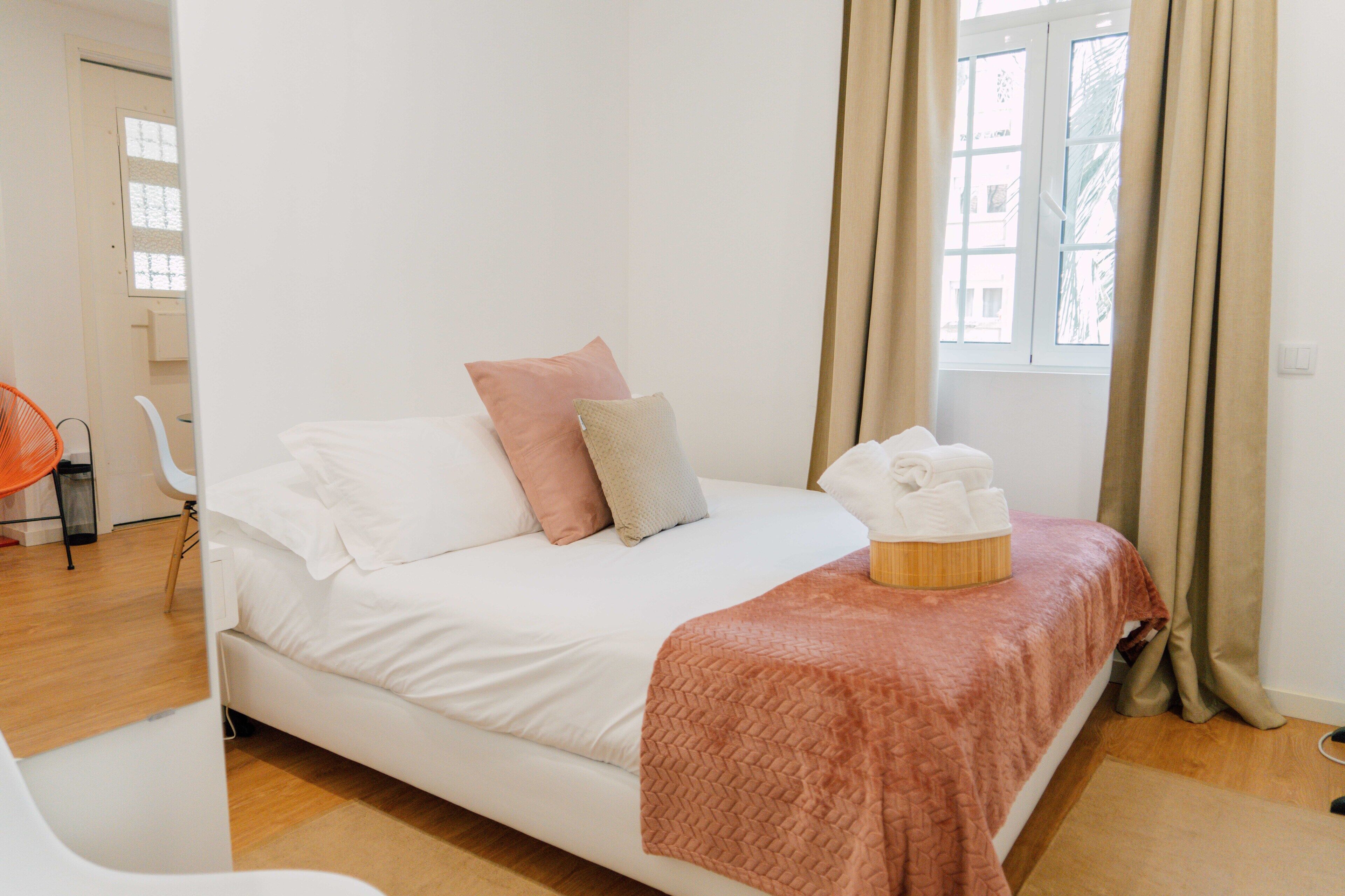 A bedroom with a bed, pillows, a blanket, and a window with curtains.