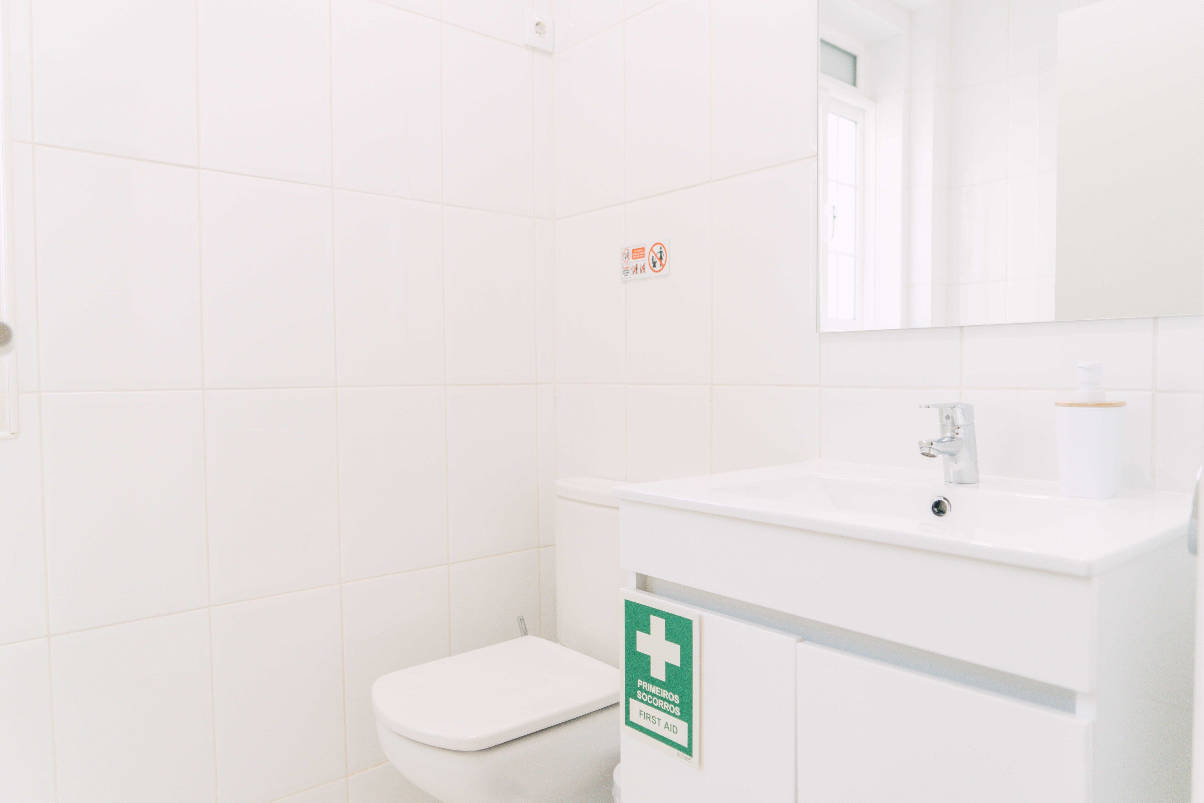 A white bathroom with a sink, mirror, and a first aid sign.