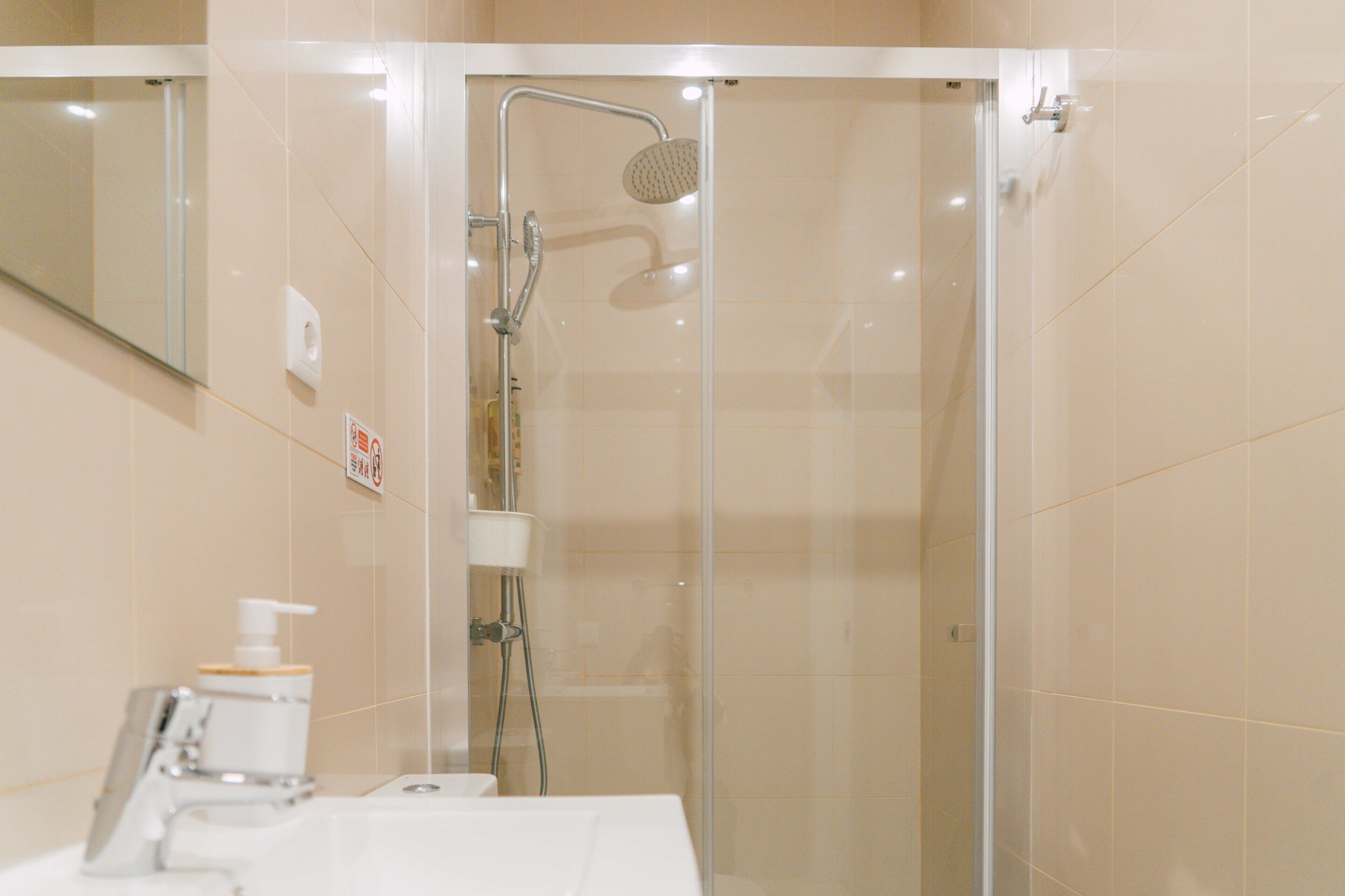 Un baño moderno con ducha envuelta en vidrio, un lavamanos con dispensador de jabón y un espejo.