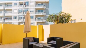 A balcony with wicker furniture, a beige umbrella, and a building in the background. - Oporto Yellow Villas   (Porto)