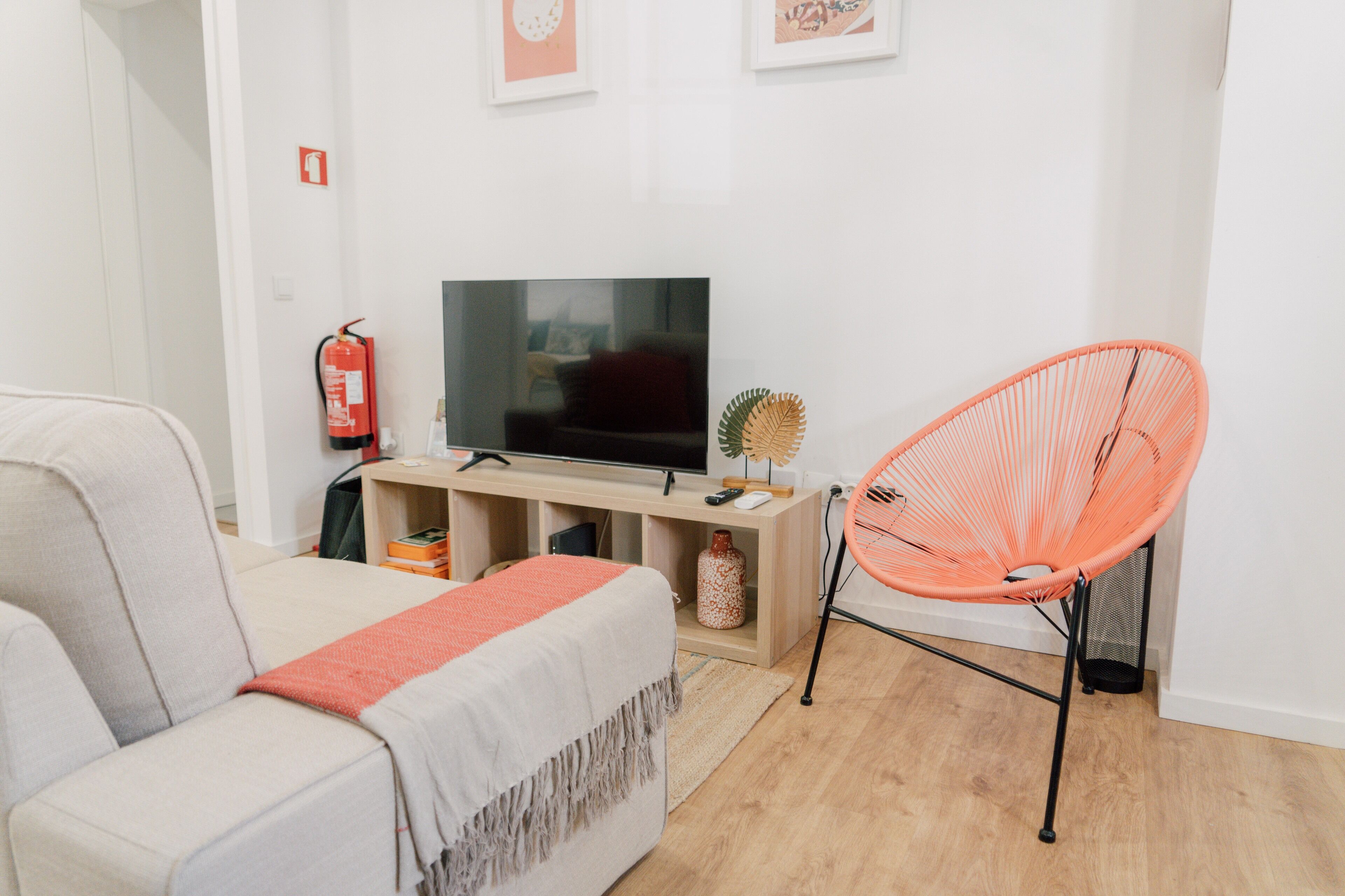 Una sala moderna con un sofá, un televisor, una mesa consola de madera y una silla naranja brillante.
