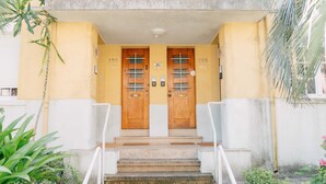 A building entrance with two wooden doors marked with numbers, a concrete staircase, and a small garden area with plants. - Oporto Yellow Villas   (Porto)