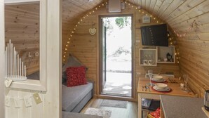 A cozy cabin interior with a wooden ceiling, a sofa with red cushions, a dining table set with plates and glasses, and a television mounted on the wall.