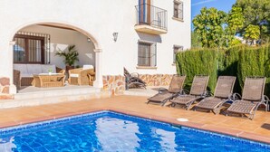 A poolside area with lounge chairs, a wicker sofa, and a small table. - Villa Isabel by Sun & Sea Homes (Moraira)