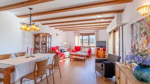 A spacious living room with a dining area, wooden beams on the ceiling, a large window, and a colorful painting on the wall. - Villa Isabel by Sun & Sea Homes (Moraira)