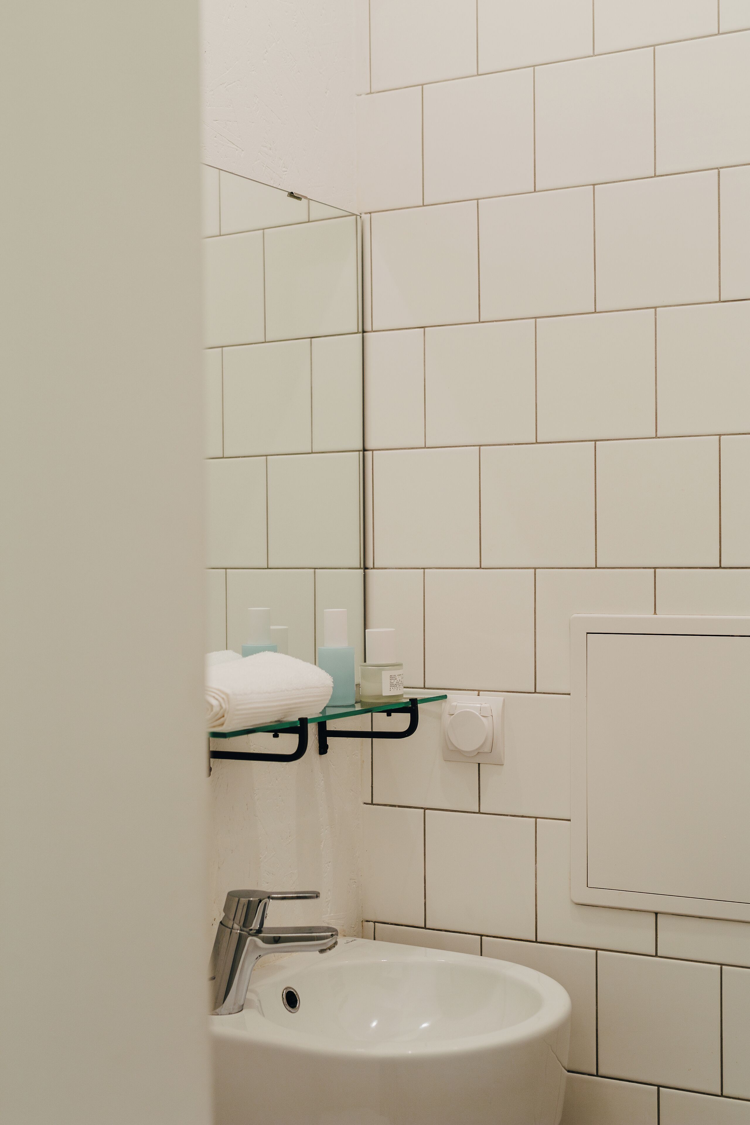 Ein Badezimmer mit einem weißen Waschbecken, einem Spiegel und einer Glasablage mit Toilettenartikeln.