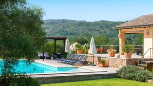 A pool area with lounge chairs and umbrellas, surrounded by greenery and a view of hills. - Villa S'airieta - Finca-Style Villa with Private Gardens Near Playa de Muro (Mallorca)