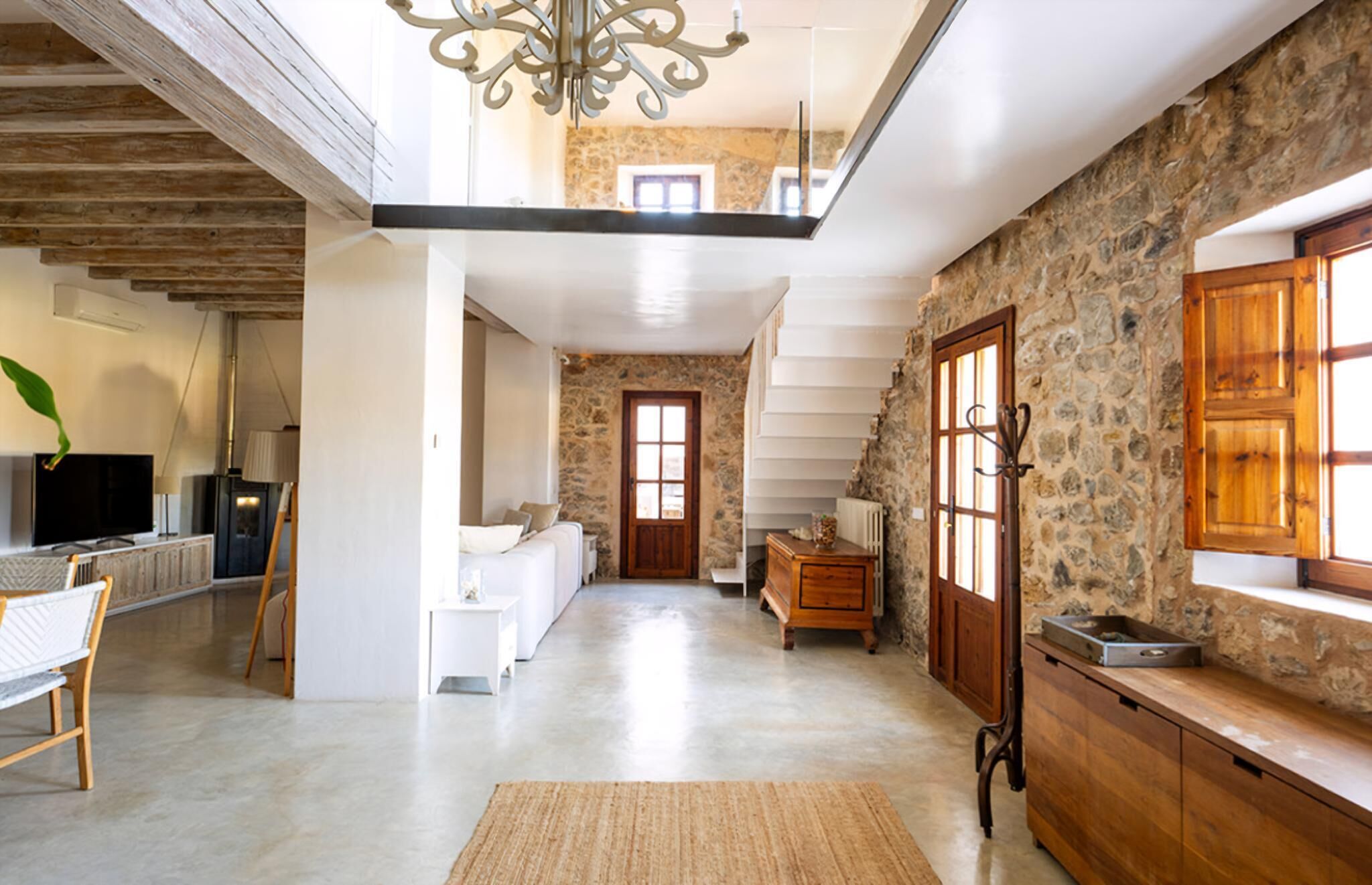 A spacious living area with a stone wall, a wooden staircase, a flat-screen TV, a sofa, and a coffee table.
