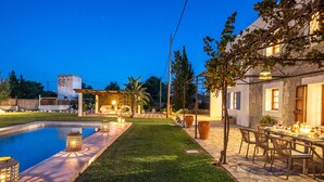 A well-lit outdoor patio area with a pool, a pergola, and a dining setup.